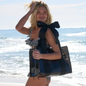 Woman holding a large black handbag on a beach #color_midnight black bow