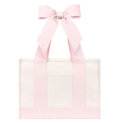 A light pink and white tote bag with wide pink shoulder straps and a large matching pink bow at the top, shown on a plain white background. #color_ballet pink bow