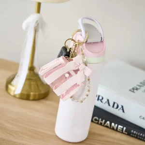 Pink shoe keychain with decorative elements on a white stand, with Prada and Chanel books in the background. #color_ballet pink bow