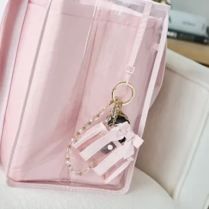Pink keychain with a camera design attached to a pink bag on a light-colored surface. #color_ballet pink bow