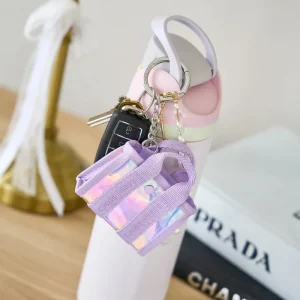 Purple holographic keychain attached to a white shoe with a blurred Prada bag in the background. #color_iridescent