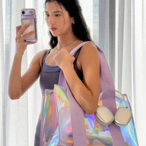 Woman holding a colorful bag with CASEMATE branding in front of a white curtain. #color_iridescent