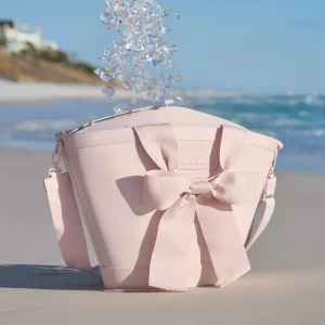 Ice cubes falling into a pink cooler with a large bow on a sandy beach with ocean and clear sky in the background #color_ballet pink bow
