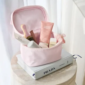 Pink cosmetic bag with skincare products on a Prada book